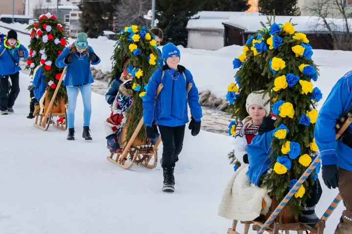 Kinder in blauen Jacken ziehen Rennbänna durch den Schnee