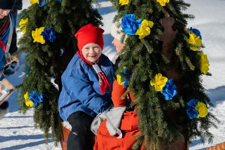 Ein Kind mit roter Mütze sitzt zwischen zwei Tannenkränzen mit Papierrosen