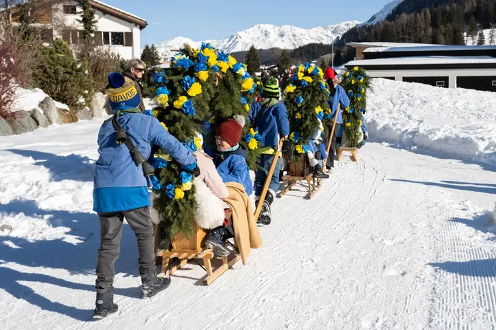 Kinder in blauen Jacken ziehen Rennbänna mit Papierrosen über den Schneeweg