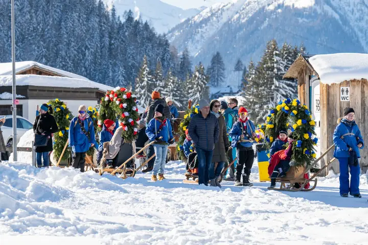 Rennbänna und Kinder vor einem Holzhaus im Schnee