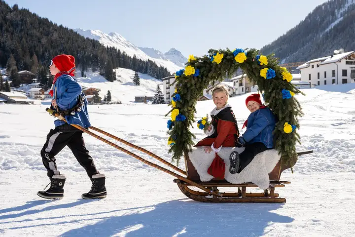 Ein Ross zieht eine Rennbänna, zwei Kinder in Tracht sitzen unter dem Rosenbogen