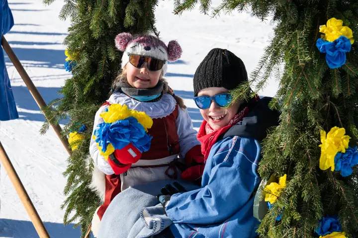 Zwei Kinder in Tracht und mit Schneebrillen zwischen Papierrosen