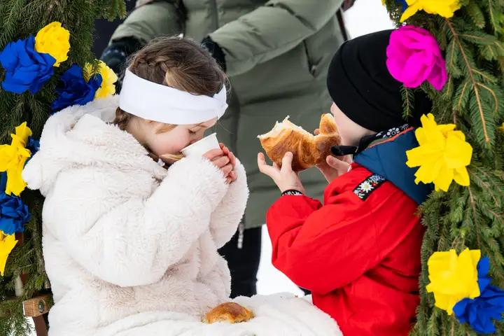 Zwei Kinder essen ein Stück Brot neben einem Tannenkranz