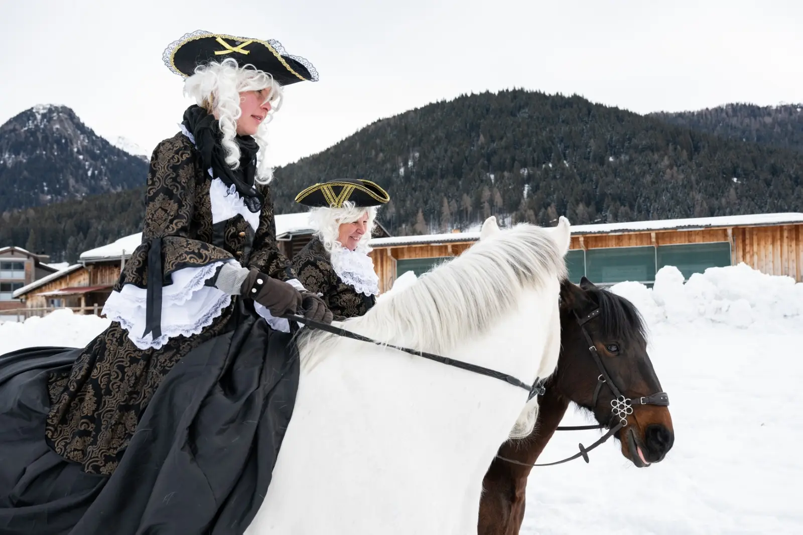 Ein Füerriiter in historischem Kostüm mit Dreispitz reitet auf einem Schimmel über den Schnee, daneben ein dunkles Pferd, dahinter die Berge