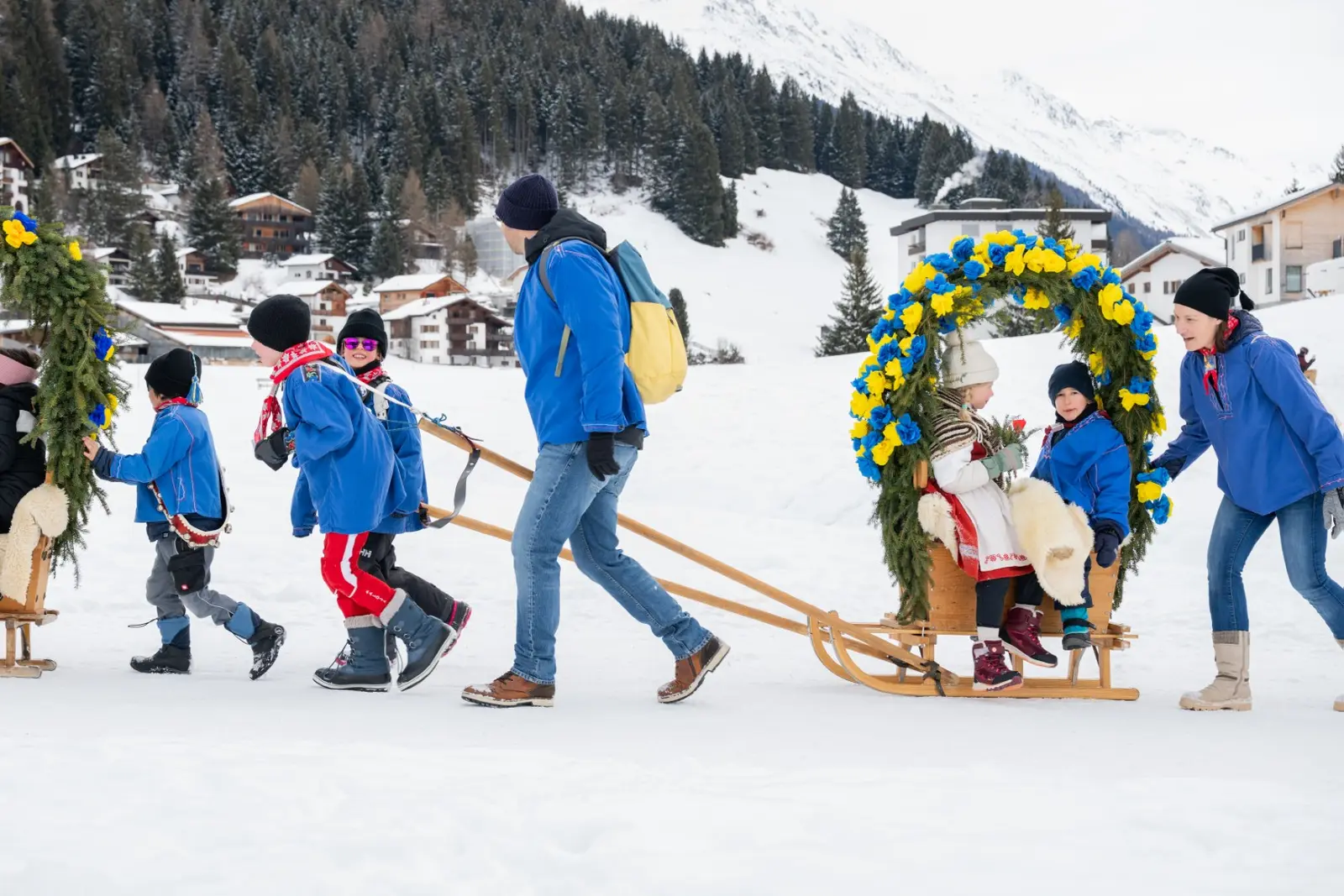 Kinder und Erwachsene ziehen eine Rennbänna mit Rosenbogen durch den Schnee