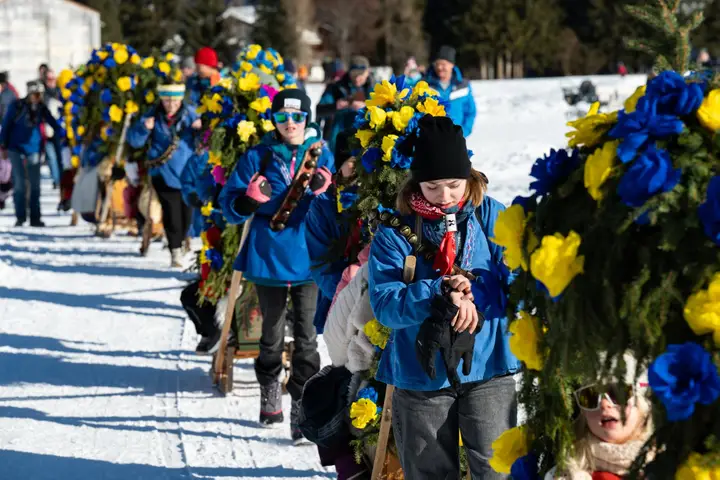 Kinder in blauen Jacken gehen neben einer Rennbänna mit Papierrosen