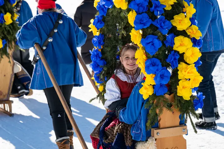 Ein Kind in Tracht vor einem Rosenbogen aus blauen und gelben Papierrosen